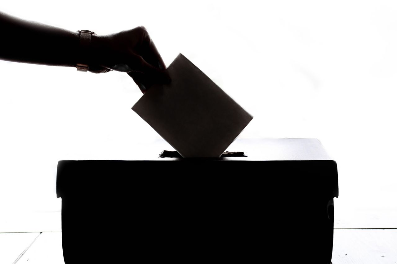 Navy and gold toned silhouette of a hand placing a ballot in a box, representing election rules in an AI usage policy