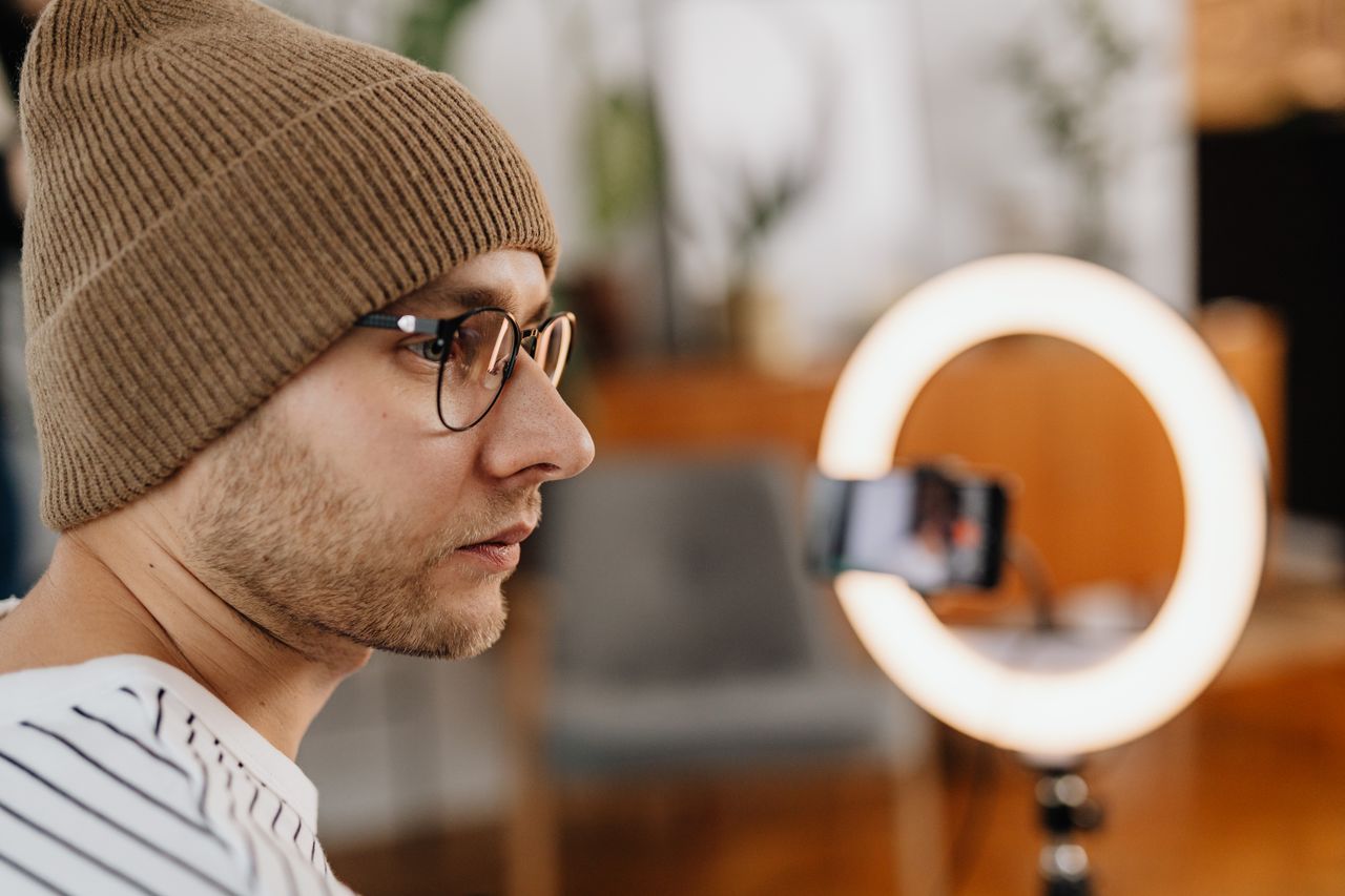 Navy and gold toned photo of a creator facing a ring light and smartphone, representing social and creator data