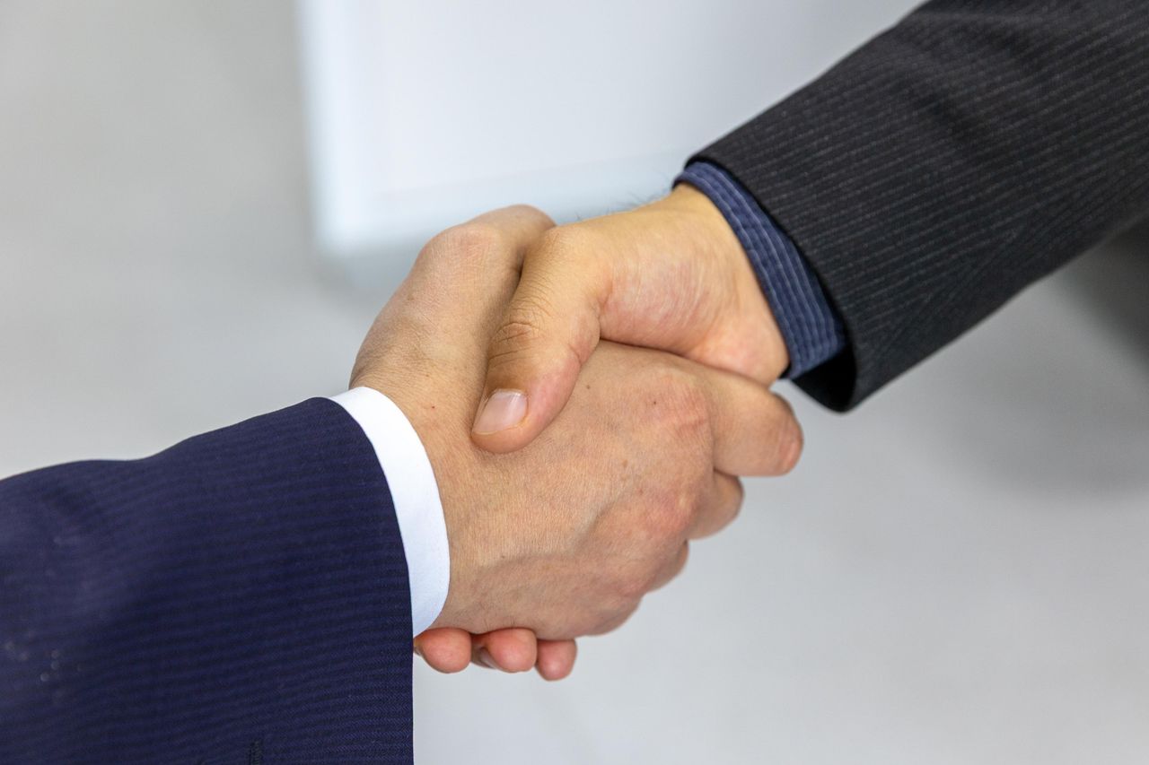 Navy and gold toned photo of a business handshake, representing personal AI agents connecting with businesses
